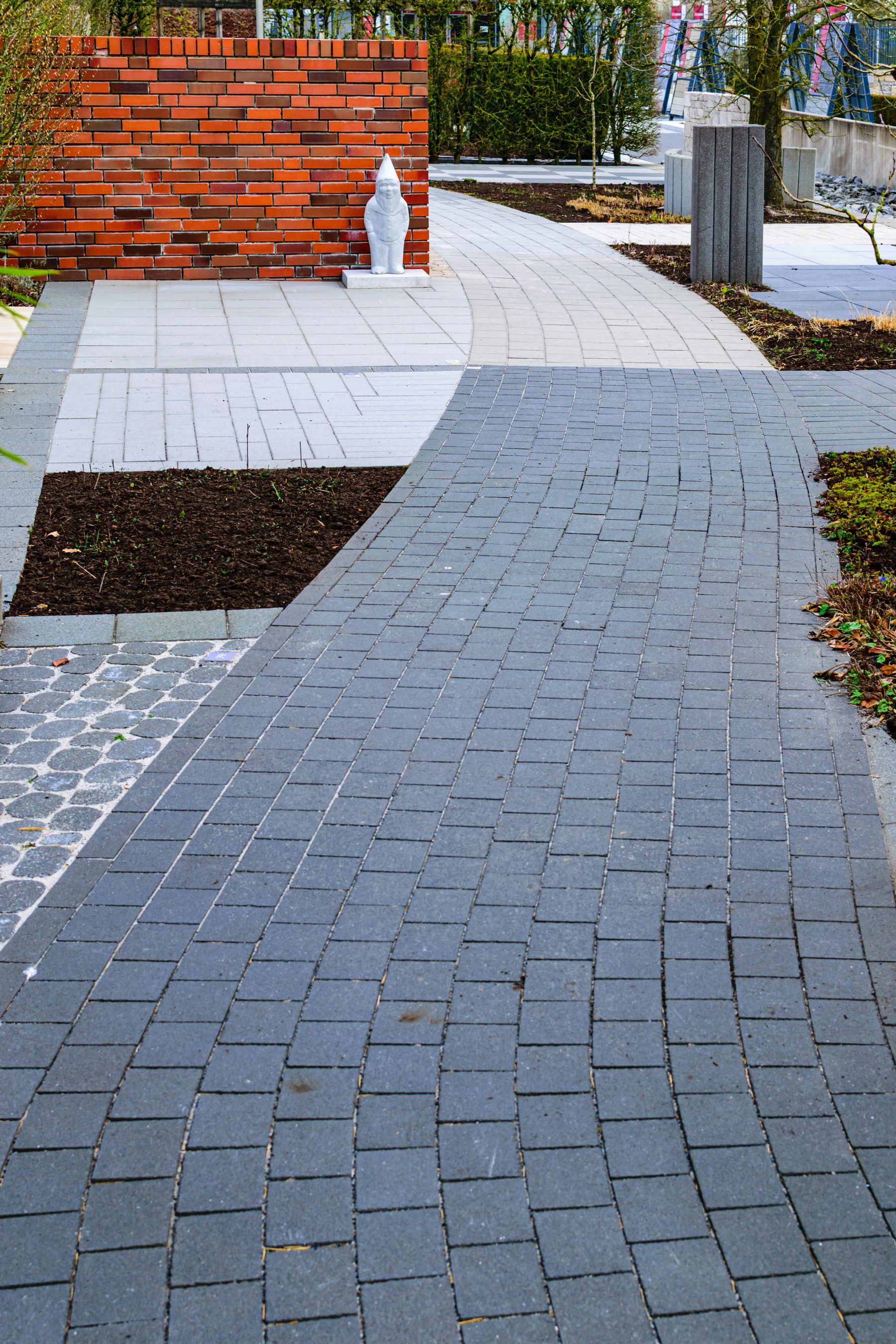 A curved red brick pathway through planted beds in a garden