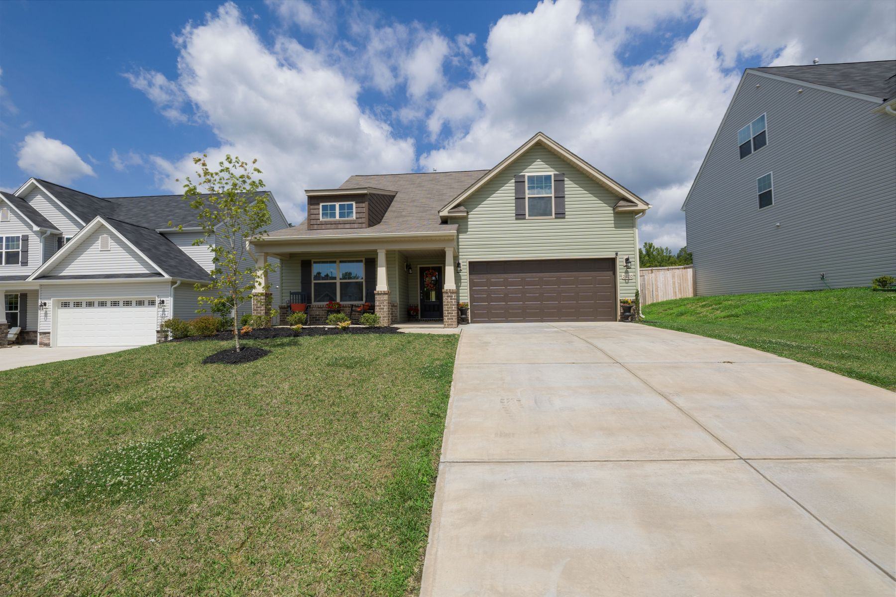 A detached suburban house with a wide driveway and lawn under a blue sky